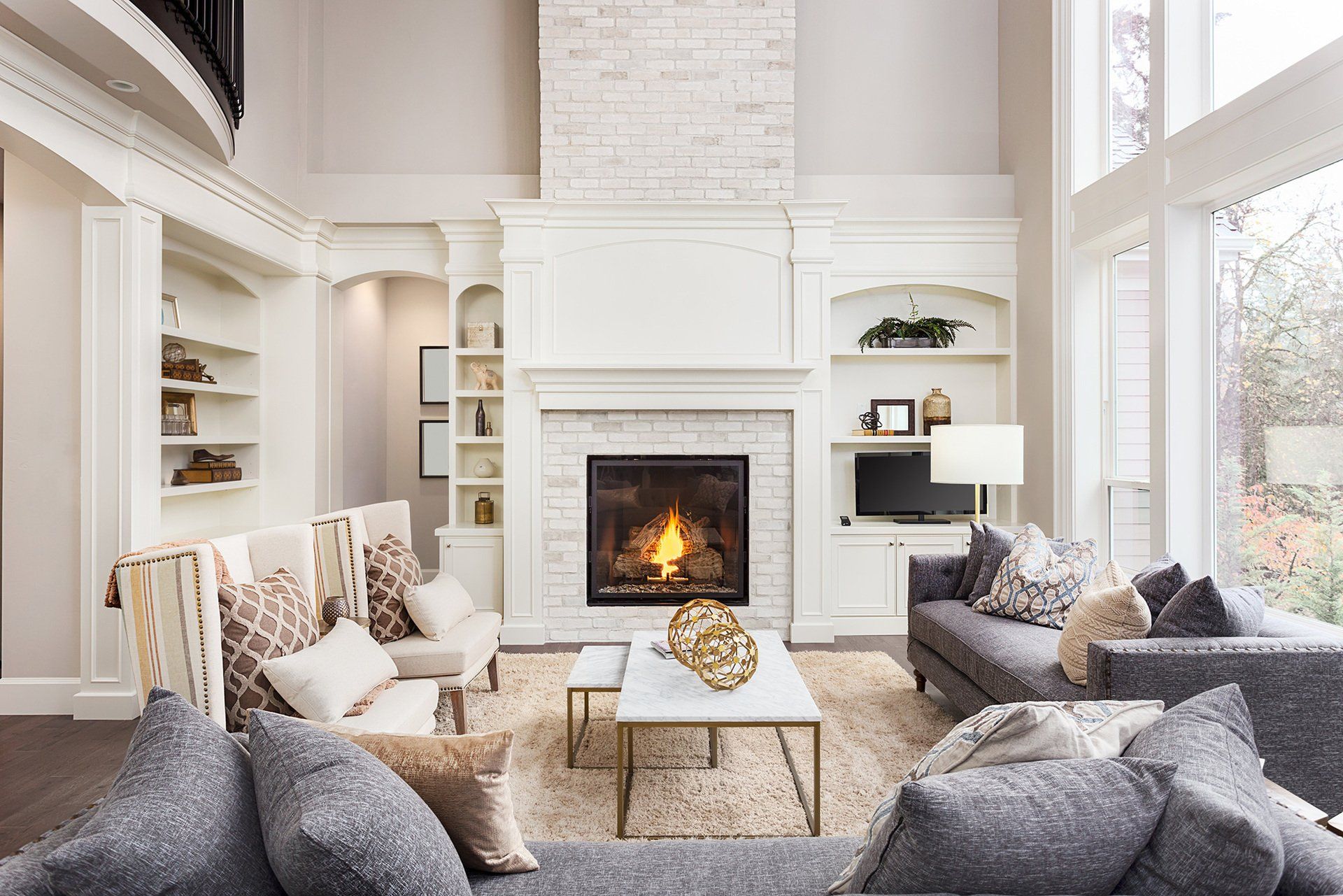 Elegant living room with fireplace, built-in shelves, gray couches, and large windows.