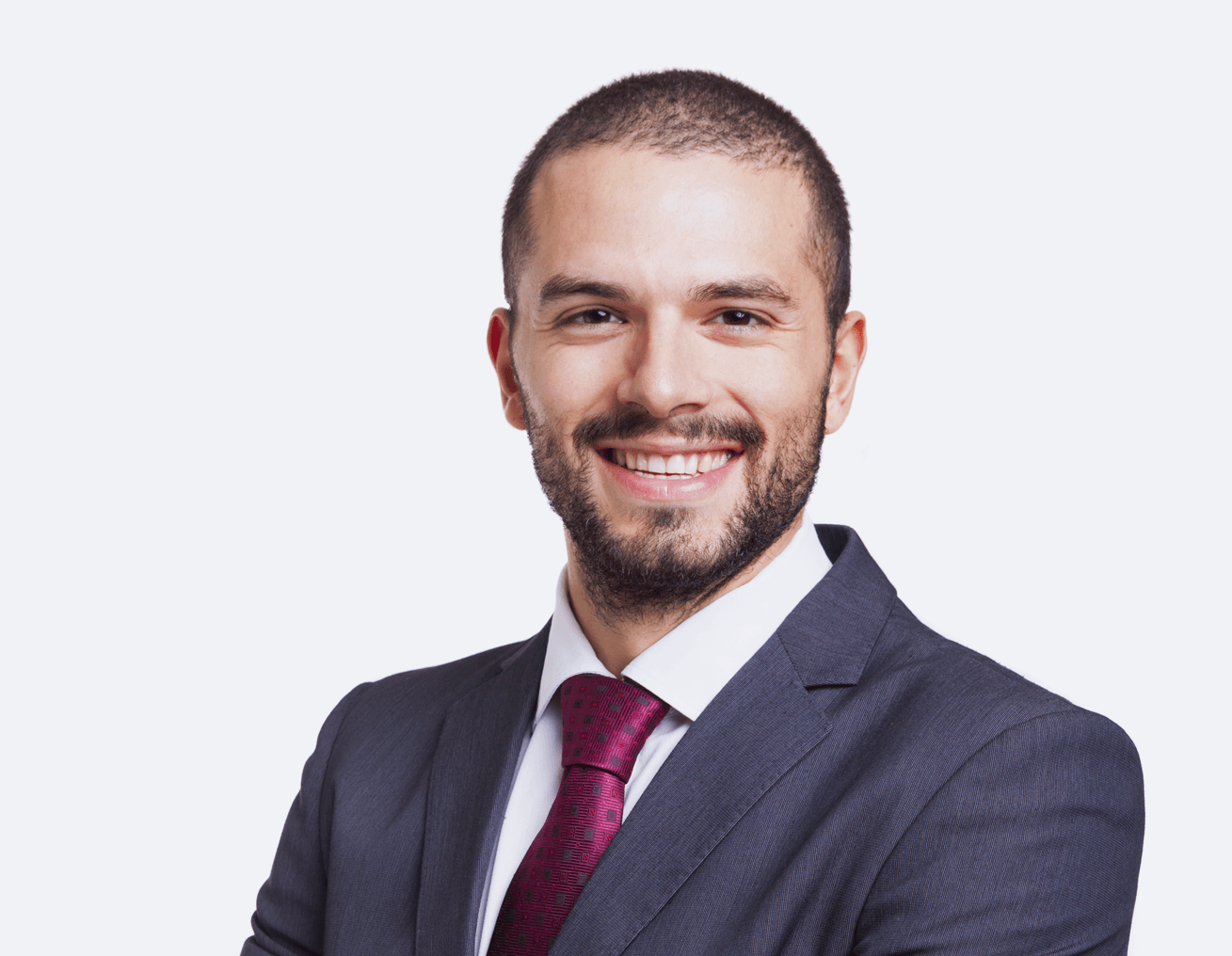 Man in a suit smiles, arms crossed, burgundy tie against a white background.