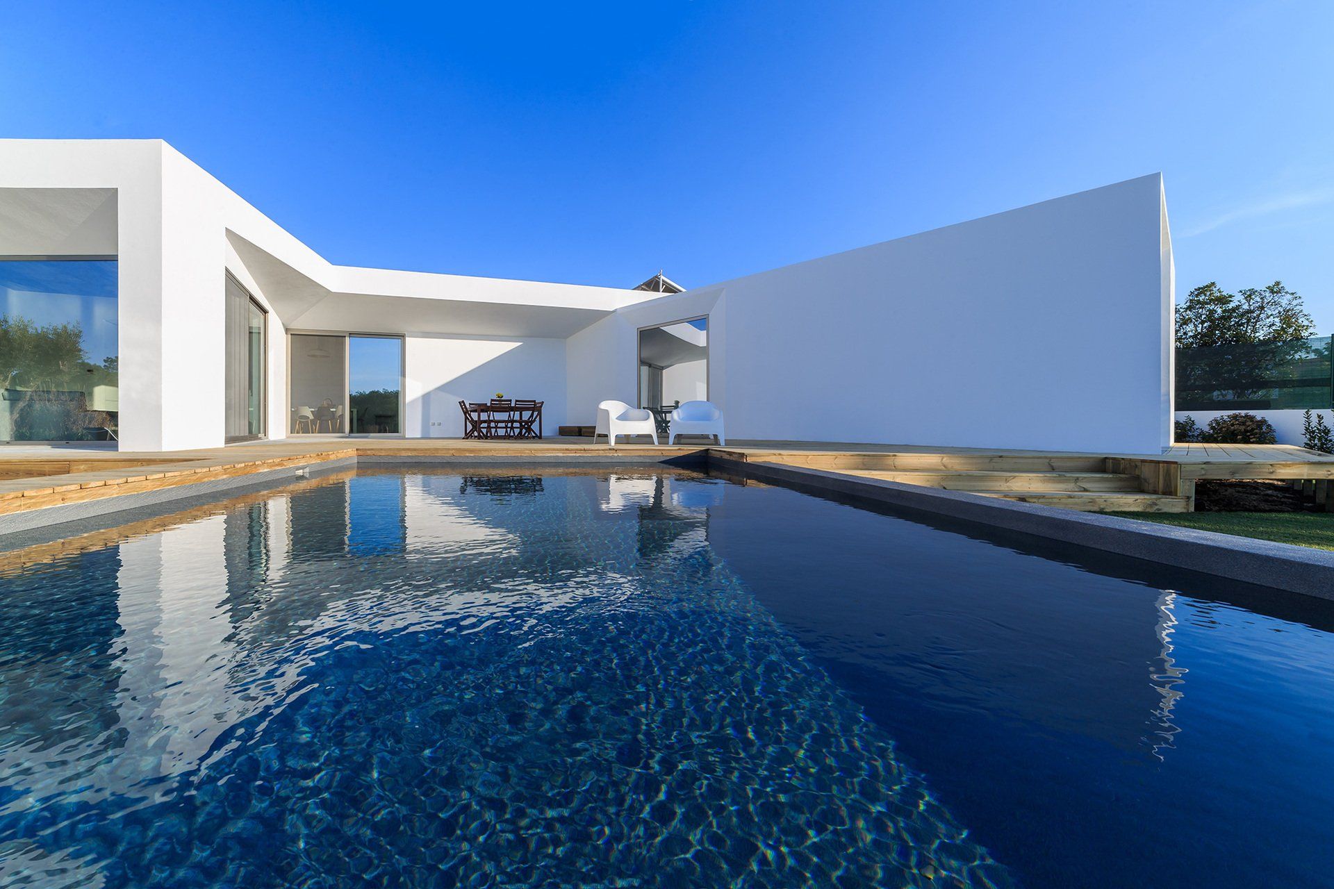 Modern white house with a pool reflecting the clear blue sky.