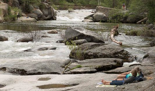 Couple relaxing by the Merced River near Swinging Bridge in Wawona