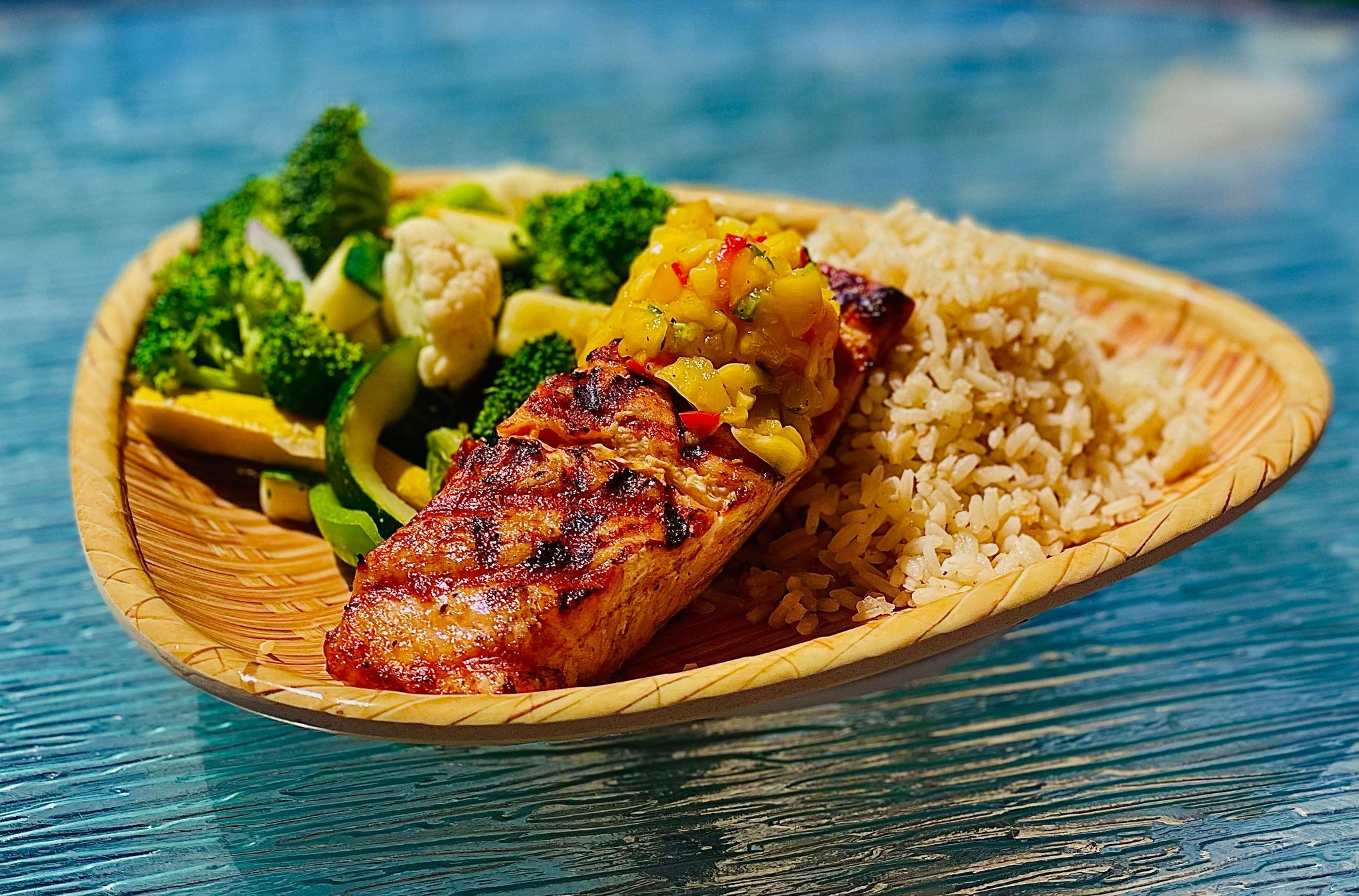 A piece of fish over a bed of rice with some vegetables on the side.