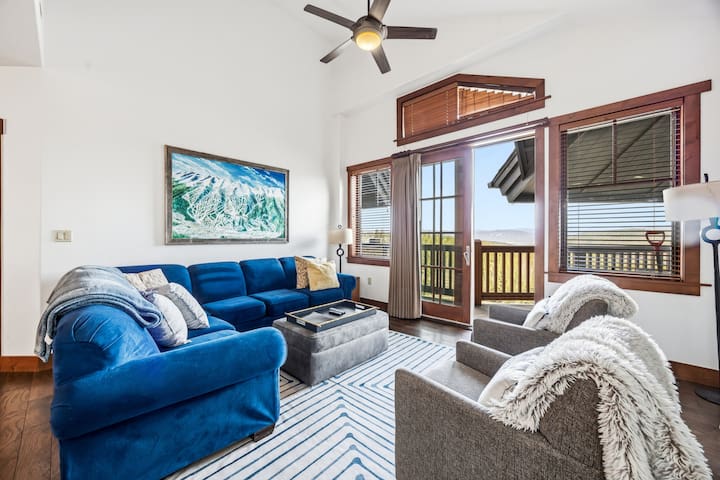 Living room of Unit 8502 at One Ski Hill Place, with vaulted ceiling, deck doors, and mountain views over Breckenridge