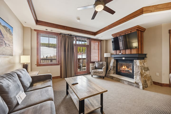 Open living and dining area of Unit 8407 at One Ski Hill Place, with a stone gas fireplace, six-seat dining table, and granite-island kitchen