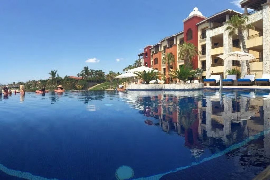 Piscina infinita en una villa de un complejo turístico de Cabo con palmeras y cielo azul