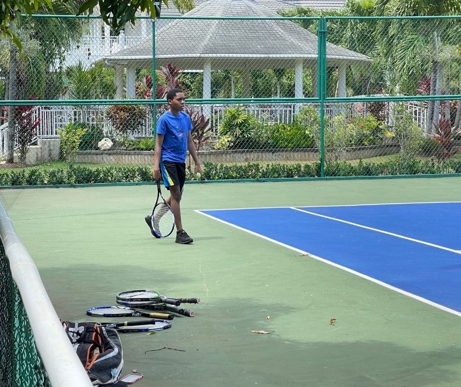 Young man on private tennis court at Mais Oui Villa in Discovery Bay Jamaica