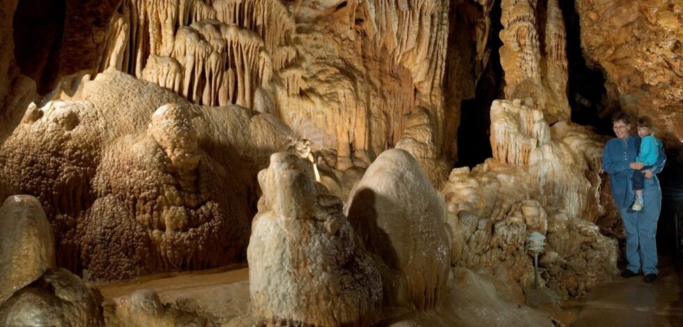 Illuminated limestone formations and stalactites inside Bridal Cave near Camdenton, with visitors standing to the right for scale