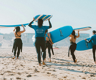Grupo de surfistas con trajes de neopreno llevando tablas de surf azules por una playa de arena