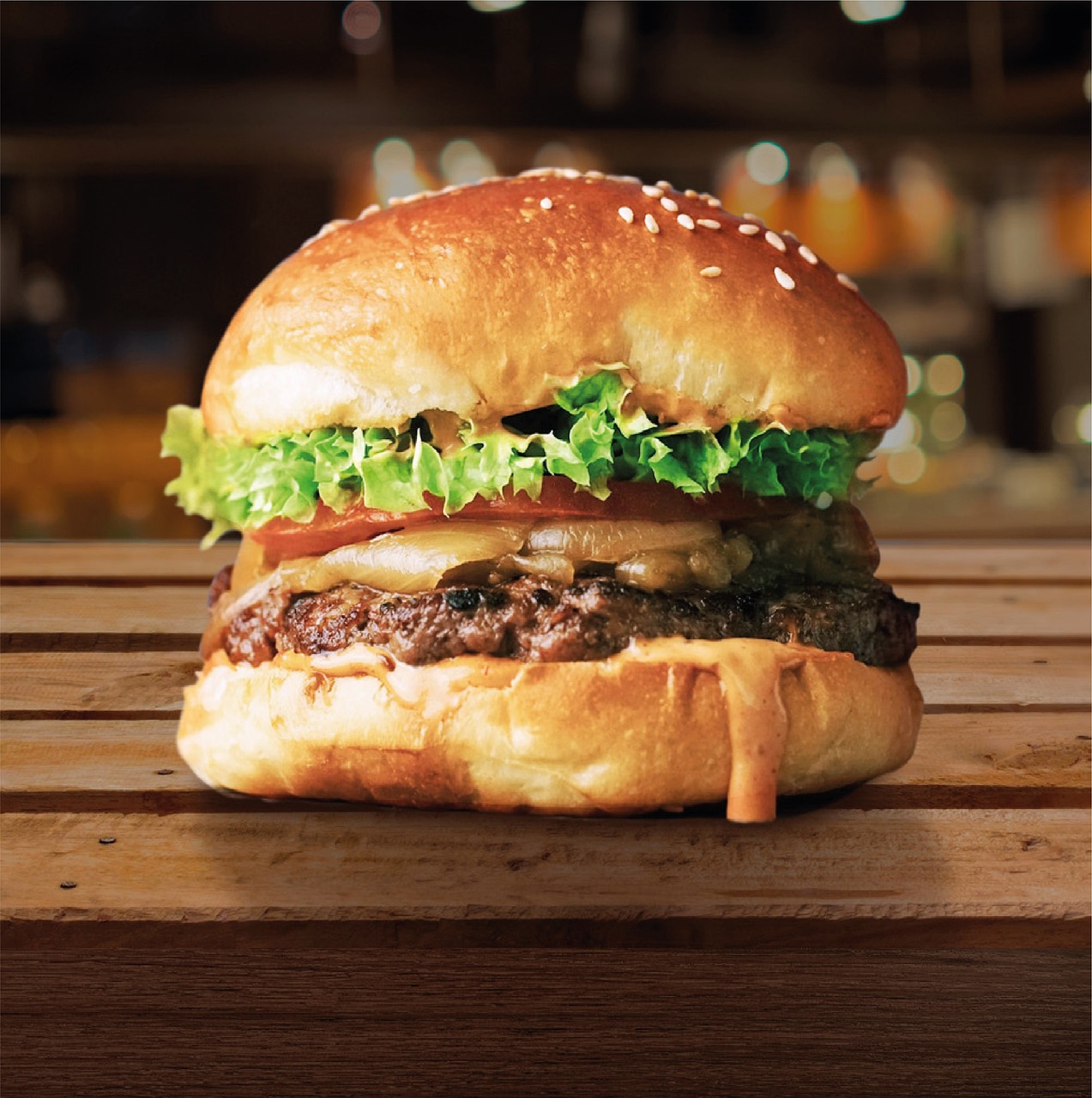 Primer plano de una hamburguesa con queso, lechuga y tomate en un pan con semillas de sésamo, sobre una superficie de madera