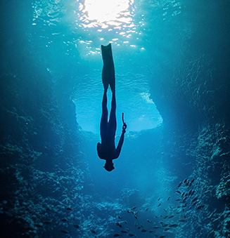Silueta de un buceador en apnea entre rayos de luz que penetran en una estrecha cueva submarina