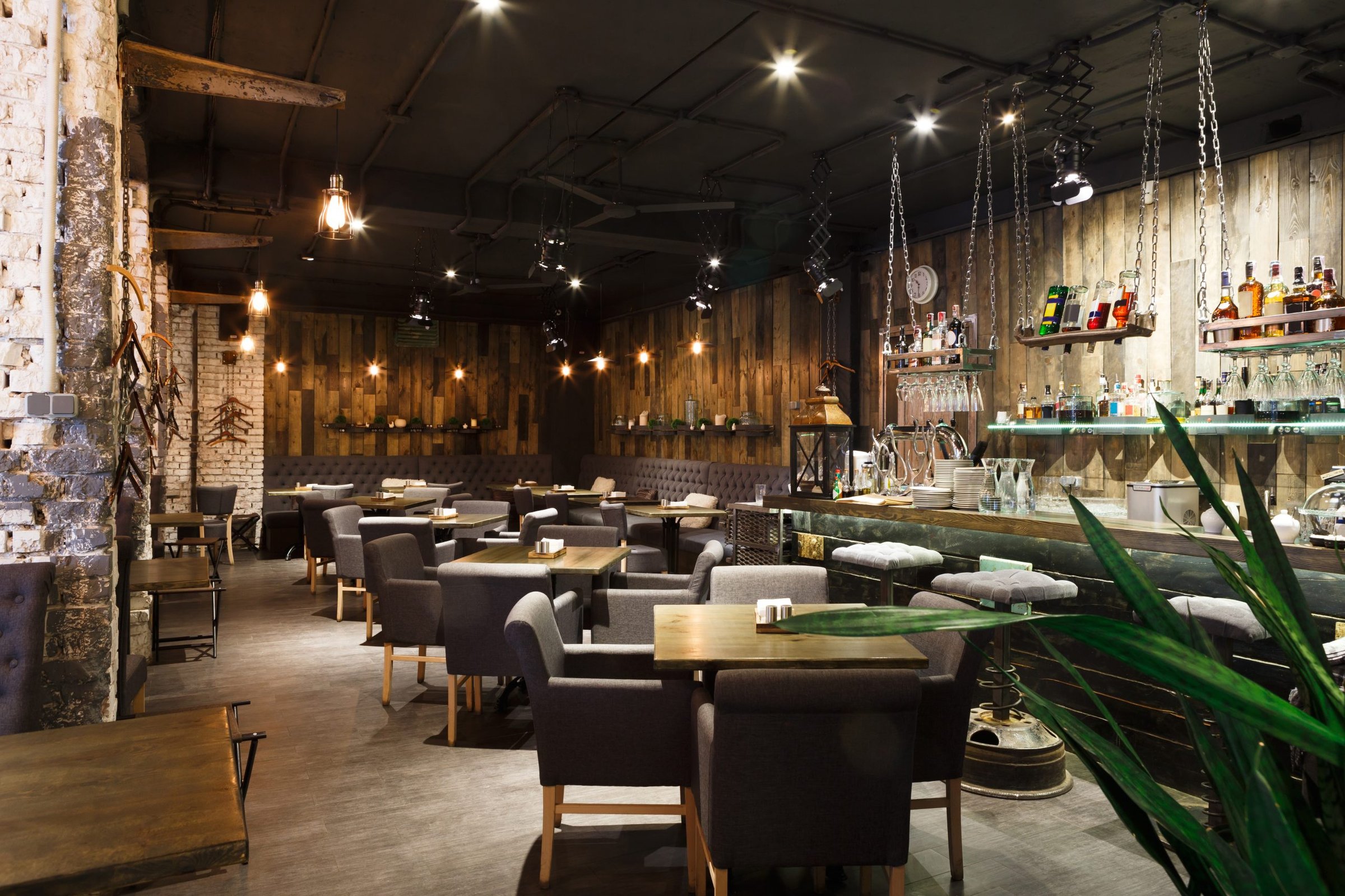 Dimly lit restaurant interior with wood-plank walls, tufted banquette seating, and pendant bulb lights above wooden tables