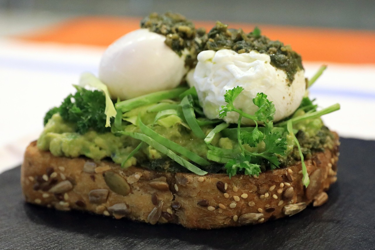Tostada de aguacate con huevo escalfado, pesto y brotes tiernos sobre una rebanada de pan con semillas