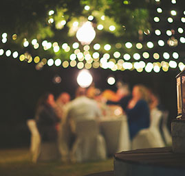 Outdoor dinner party at night with string lights glowing above guests seated at a long table