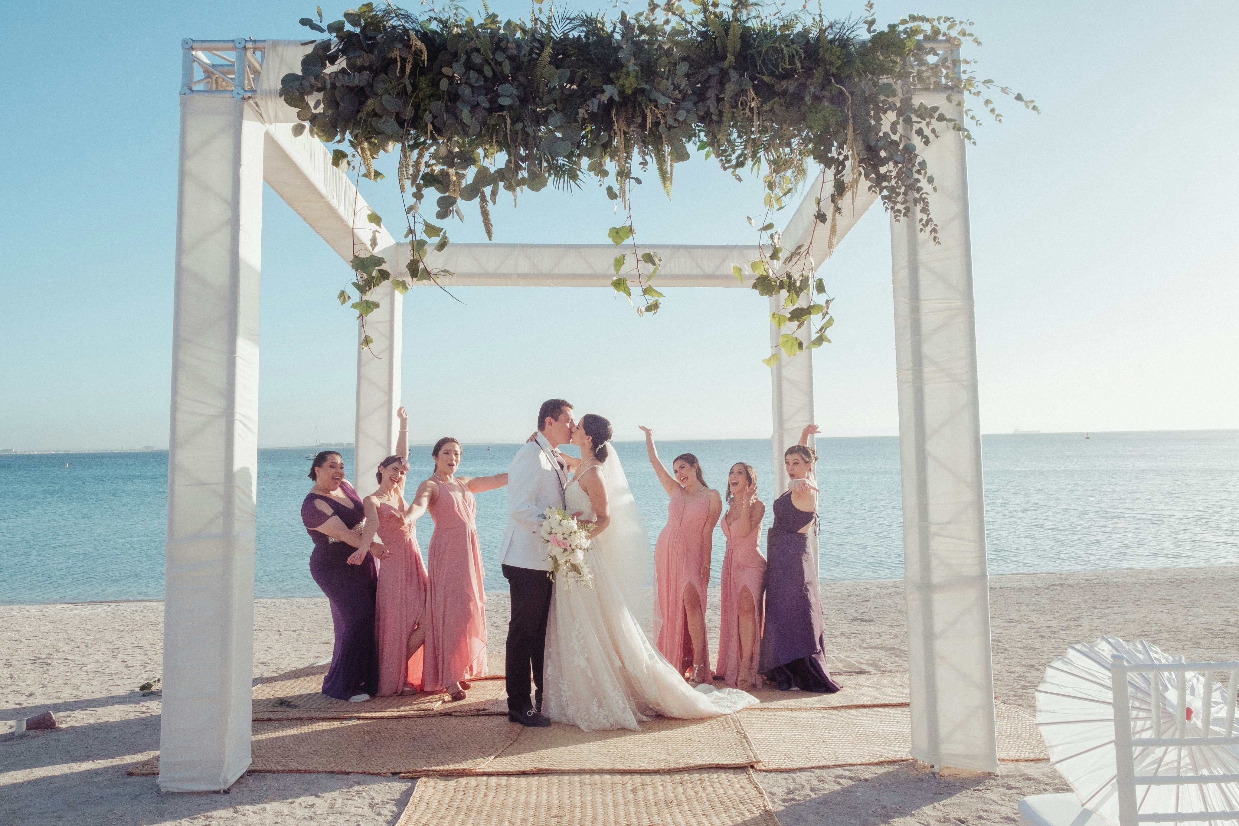 Ceremonia de boda en la playa con sillas blancas y un arco floral sobre la arena junto al mar