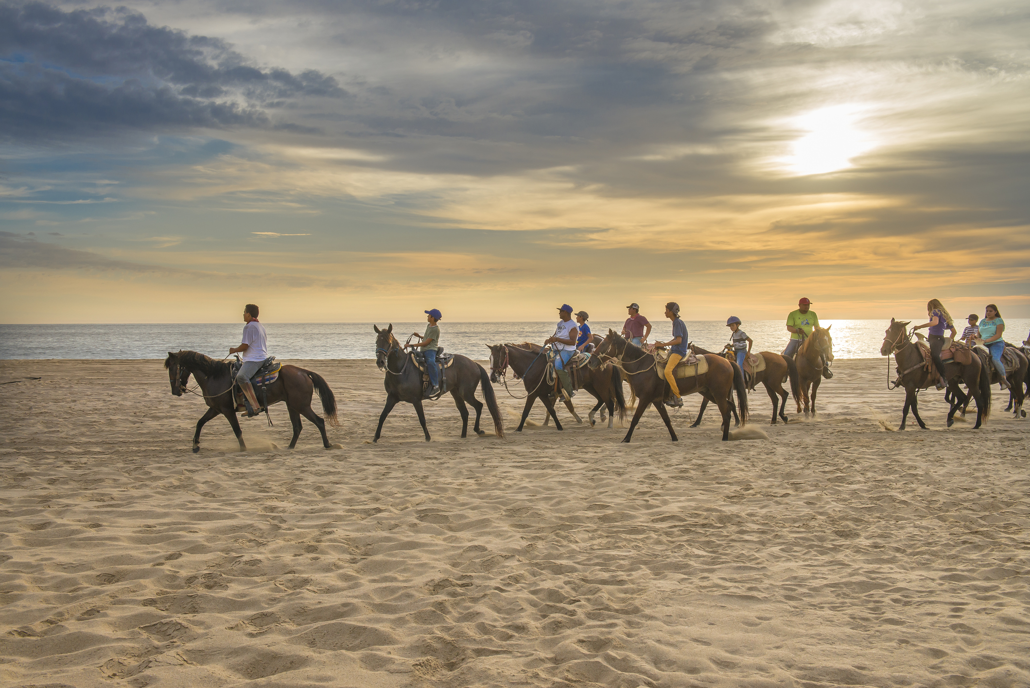 Grupo de jinetes a caballo recorriendo una playa de arena al atardecer