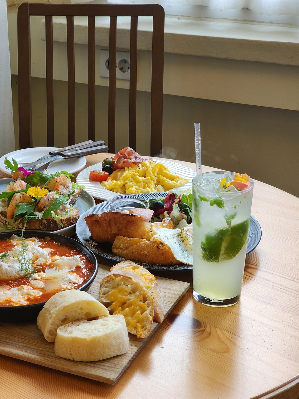 Brunch servido en una mesa de madera con huevos, tostadas con camarones, huevos revueltos, pan y un mojito