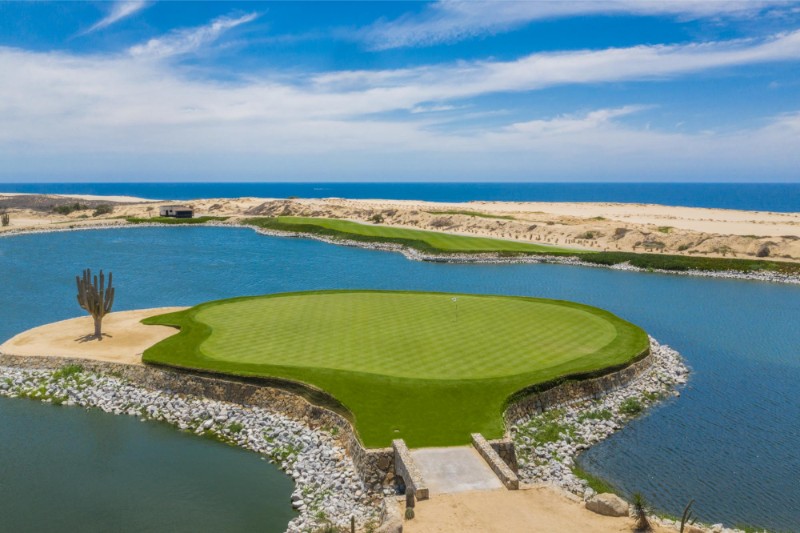 Green de golf en una isla rodeada por un lago, con dunas de arena y el mar de Cortés al fondo