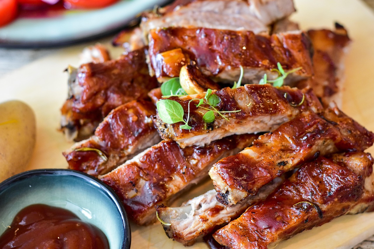 Costillas a la barbacoa glaseadas con hierbas sobre una tabla de madera junto a un cuenco pequeño con salsa