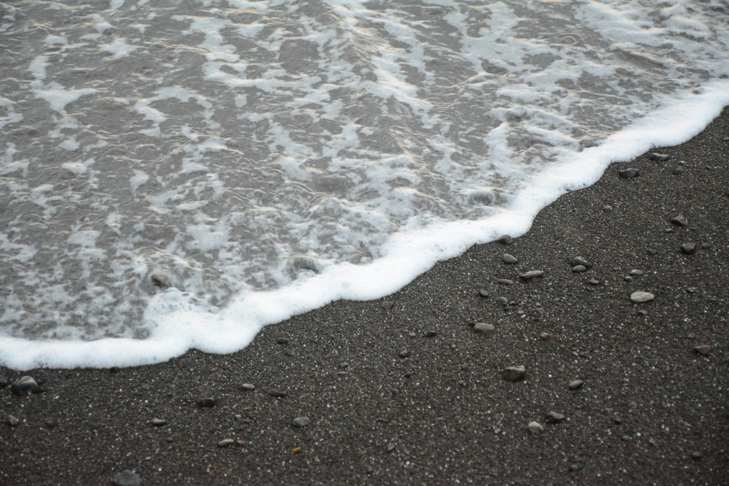 The calm water and dark sand curve of Playa Herradura on Costa Rica's central Pacific coast, with forested hills behind the beach