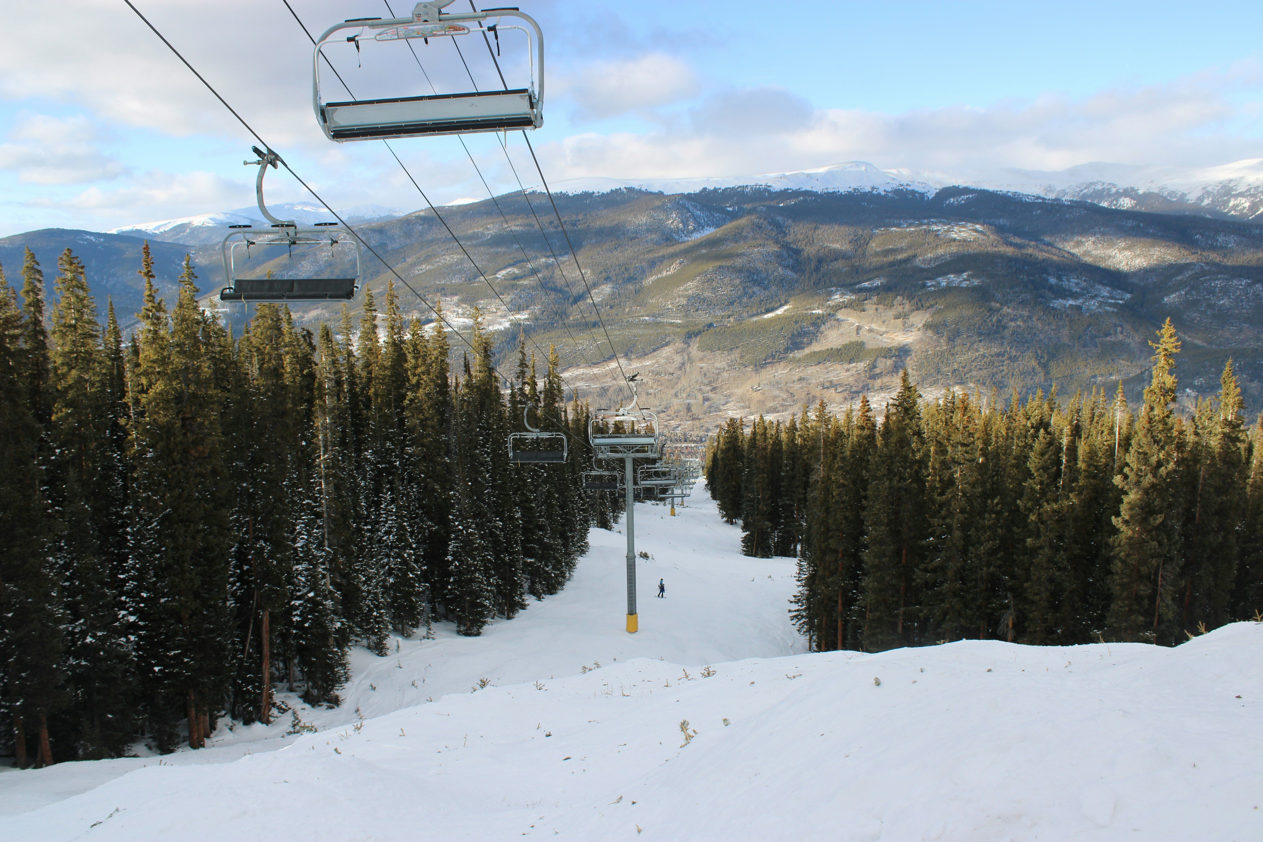 Ski lift chairs ascending a snow-covered run through pine trees