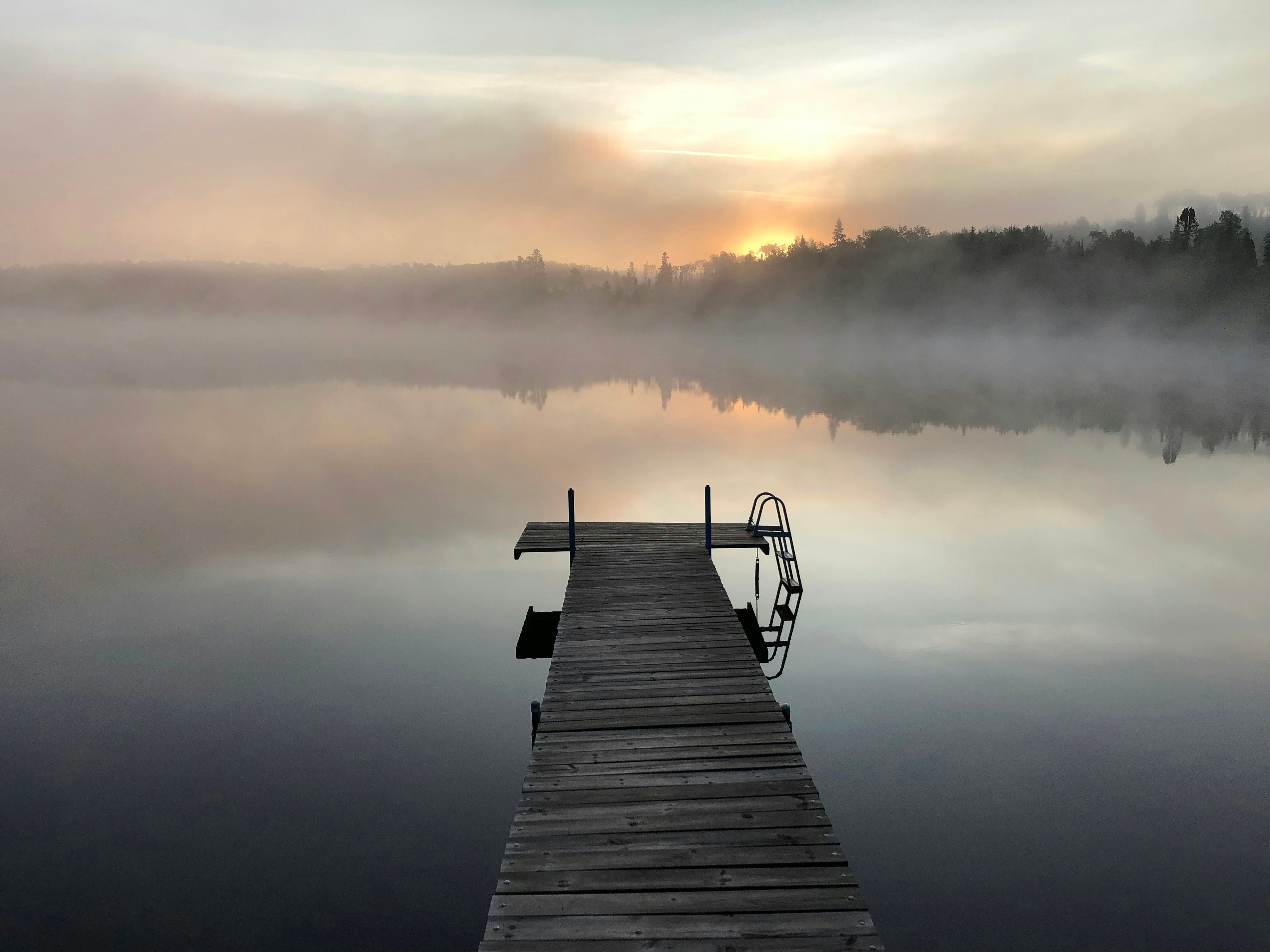 Misty dock at sunrise with fog rising off a pine-ringed lake