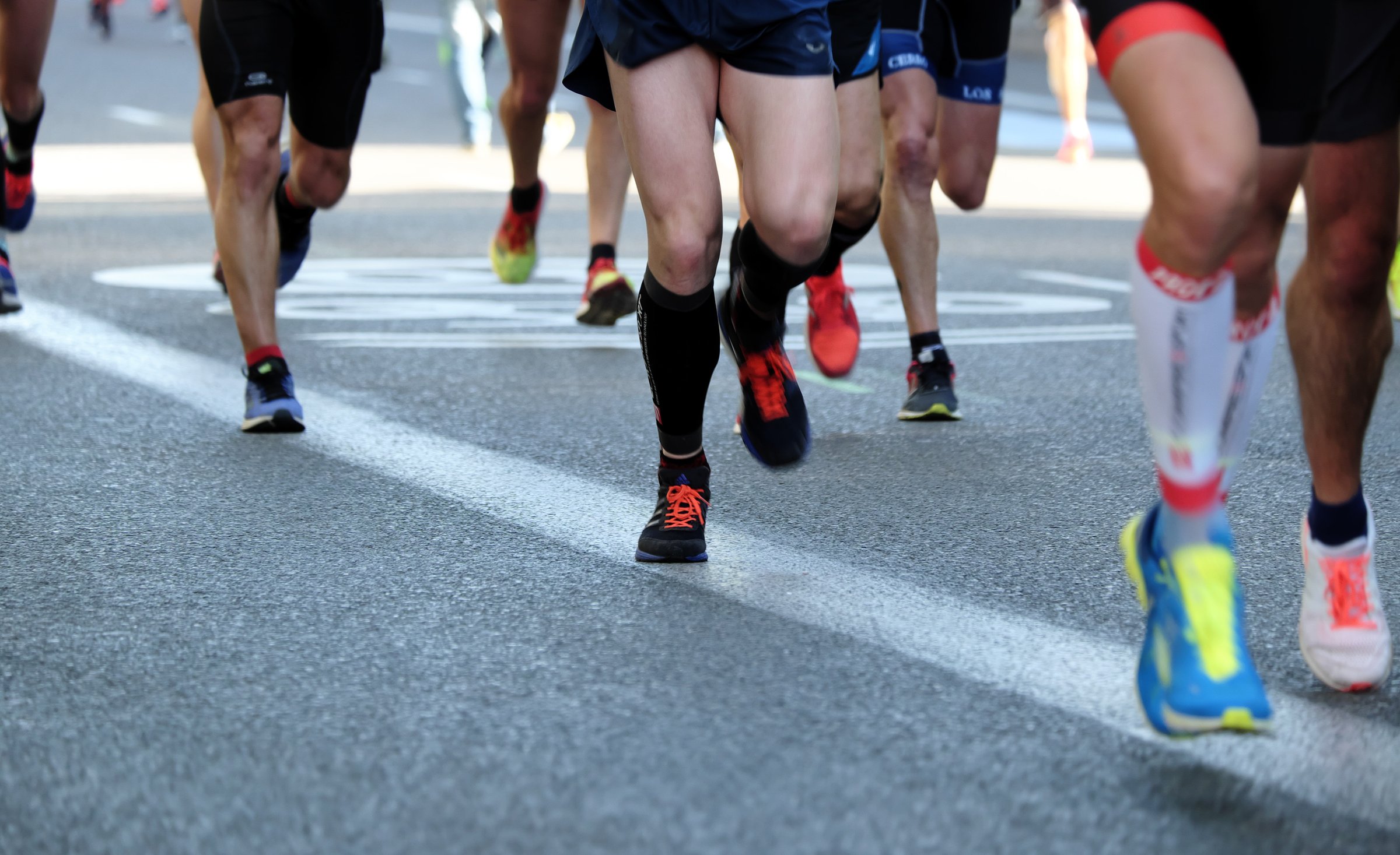 lower legs of runners with bright running shoes and compression sleeves running on black paved road