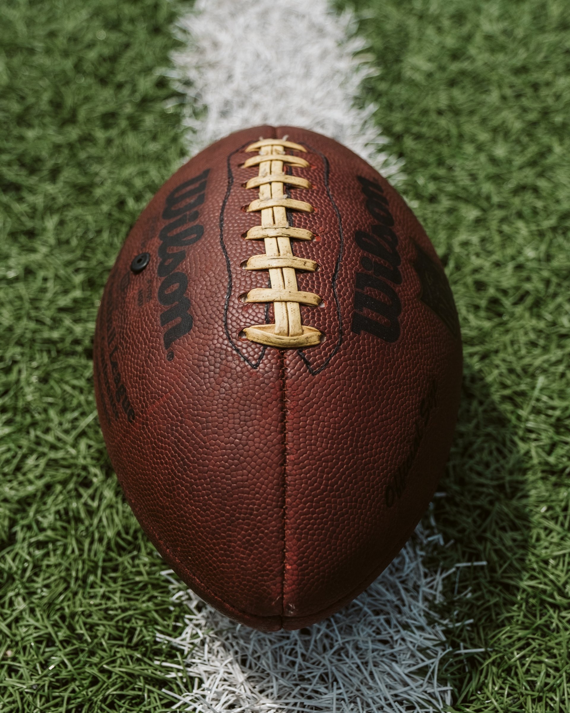 brown, leather football on green field with white lines