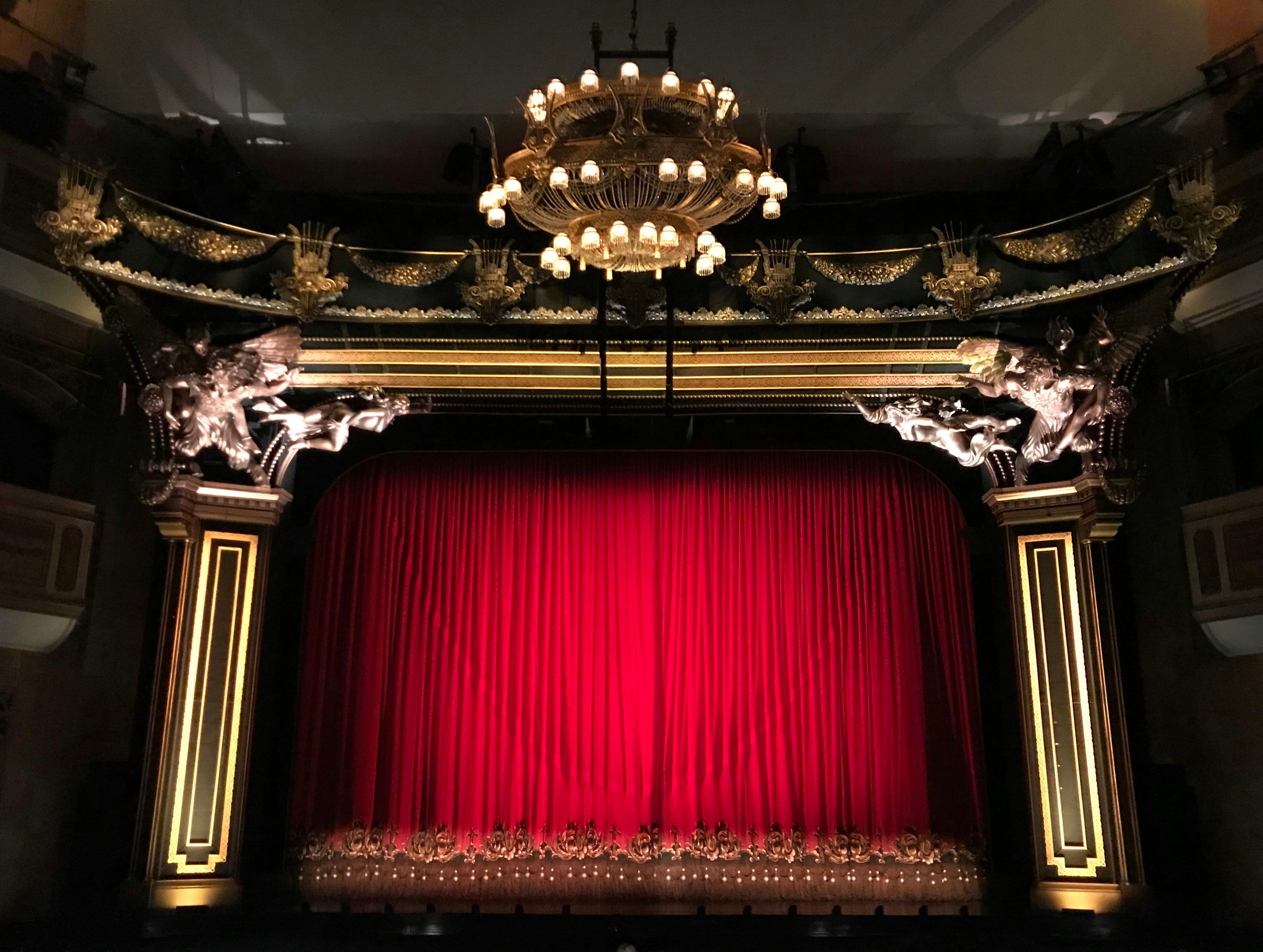 Ornate performing arts theater with chandelier and red curtain