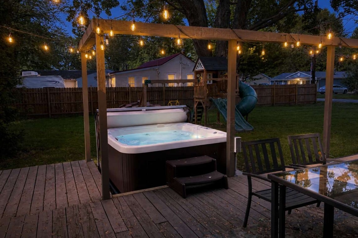 Inviting short-term rental backyard with hot tub, outdoor seating, and colorful evening lighting for guests