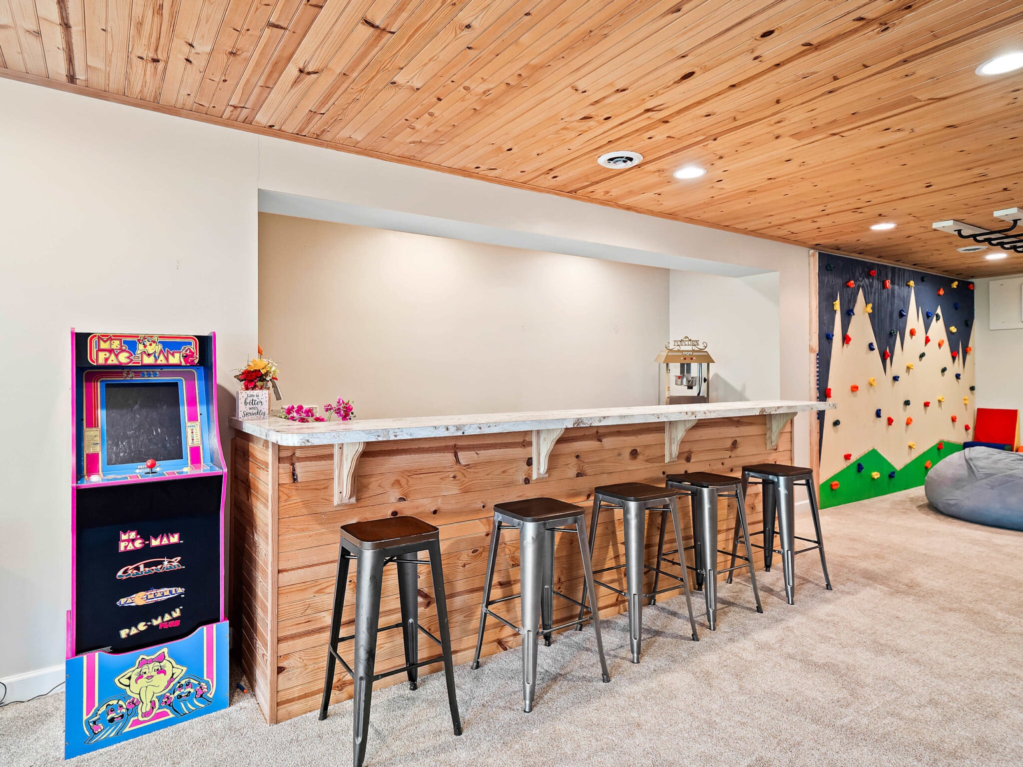 Family entertainment basement featuring a custom bar, arcade game, climbing wall, and recreation space inside a vacation rental