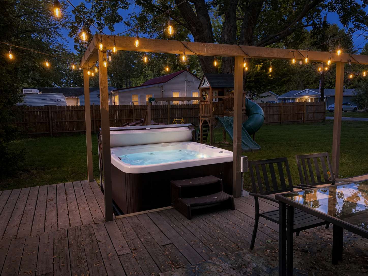 Inviting short-term rental backyard with hot tub, outdoor seating, and colorful evening lighting for guests