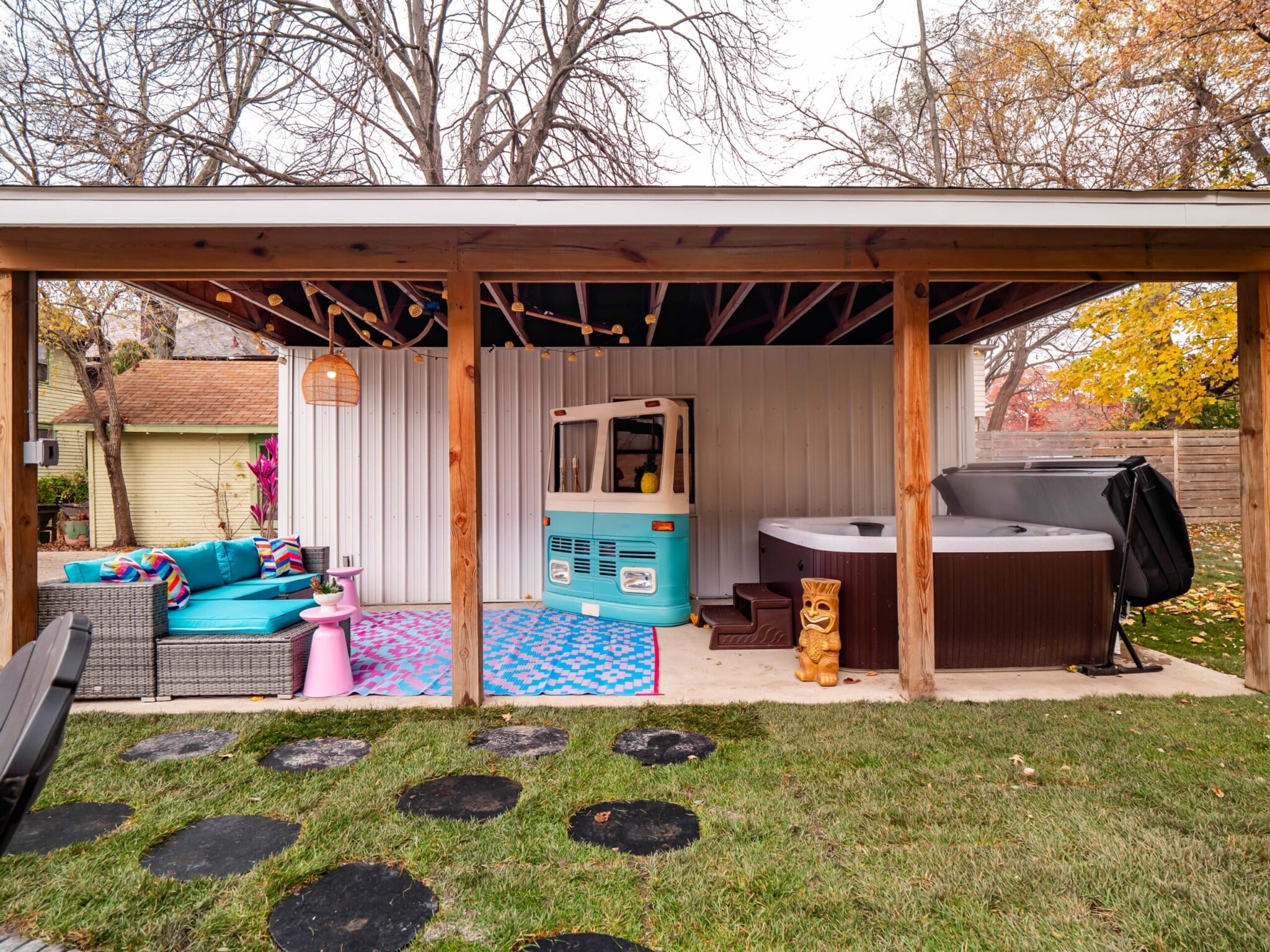 Resort-style short-term rental backyard with hot tub, fire pit seating, VW bus mini bar, string lights, and outdoor entertainment space