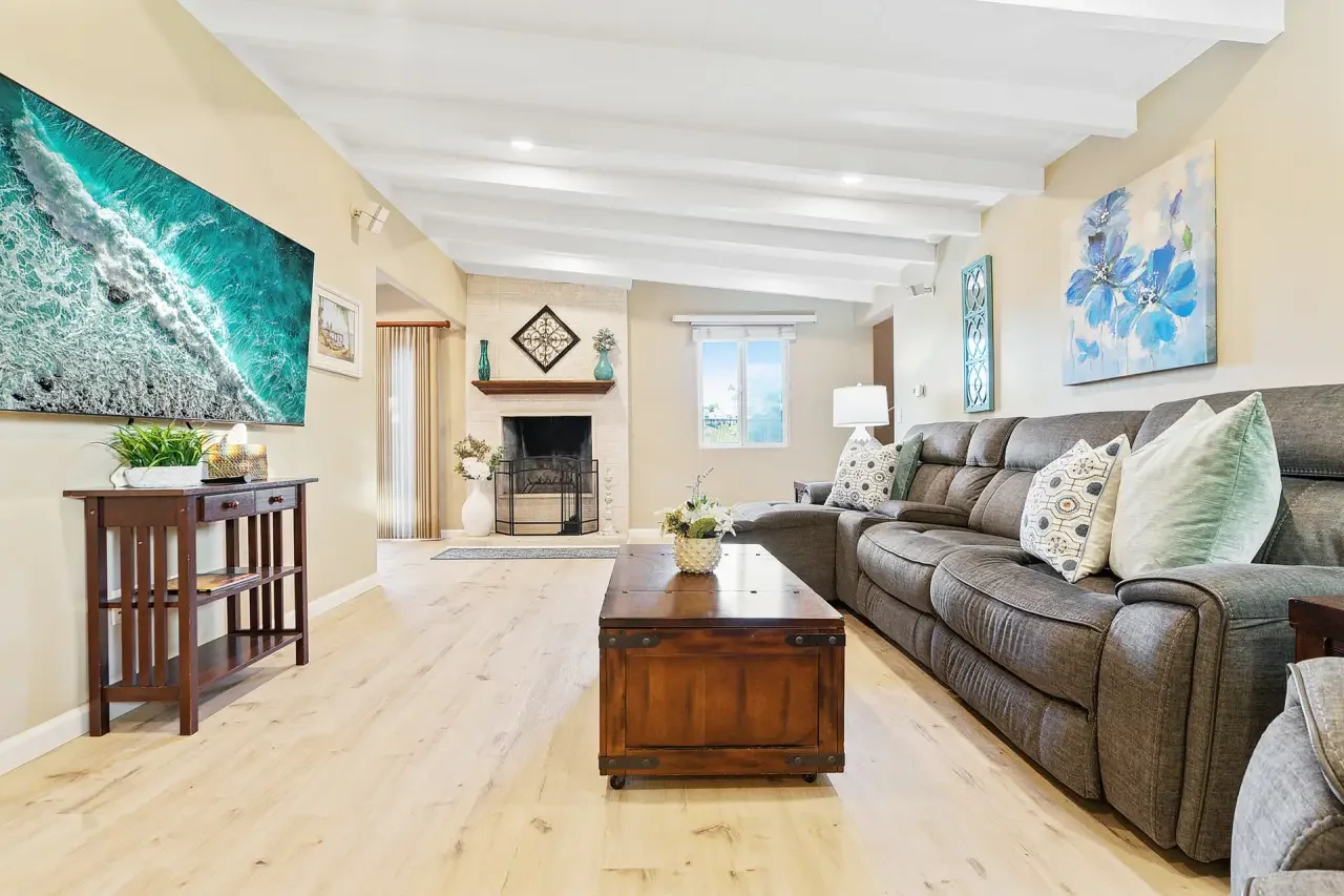 Coastal living room with gray sectional, fireplace, and ocean wave artwork in San Diego rental