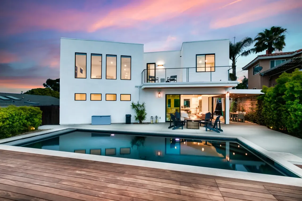 Modern San Diego real estate exterior with illuminated pool, glass doors, and contemporary architecture at dusk