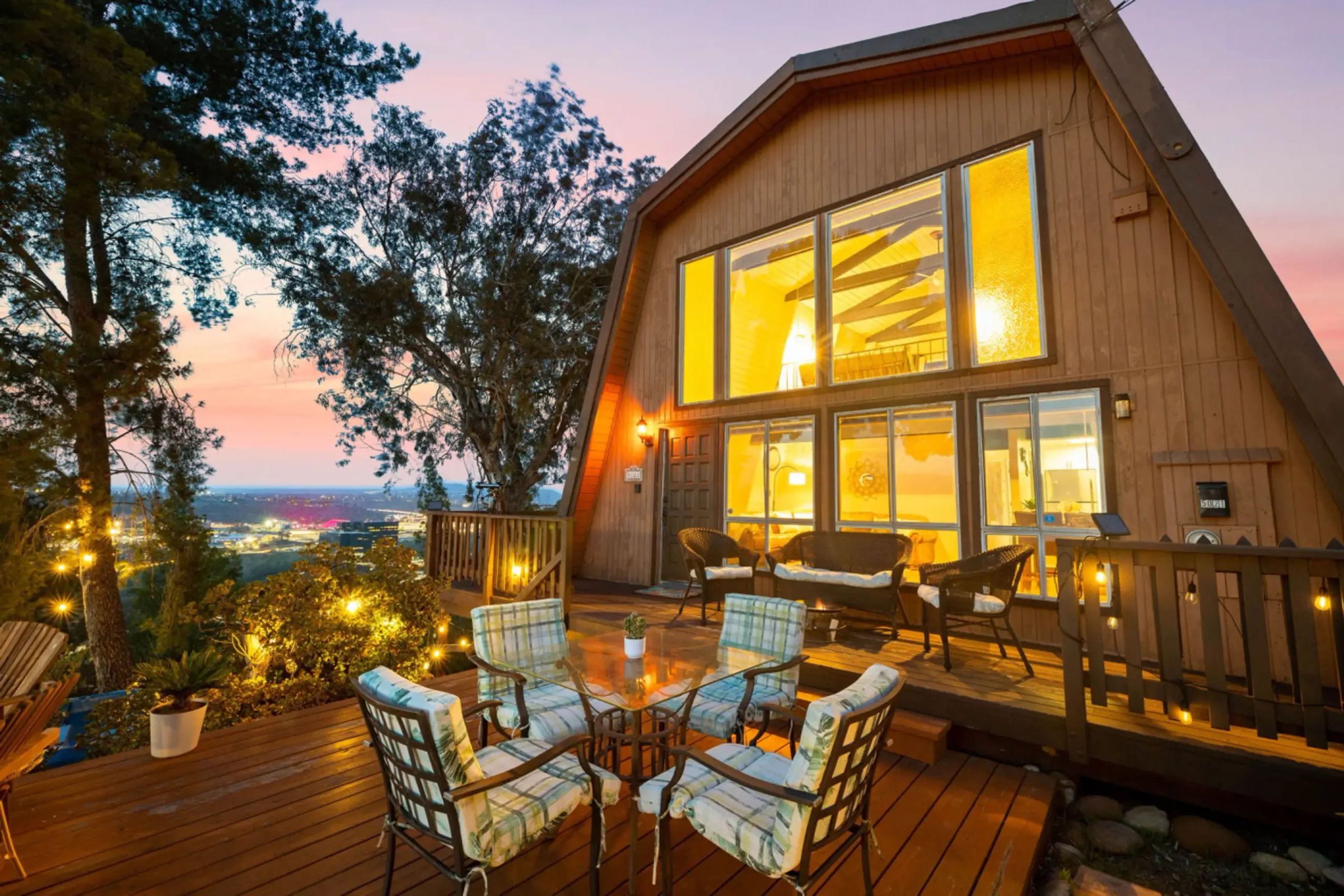 Modern A-frame cabin with illuminated windows and wooden deck overlooking panoramic valley views at dusk, ideal for Mission