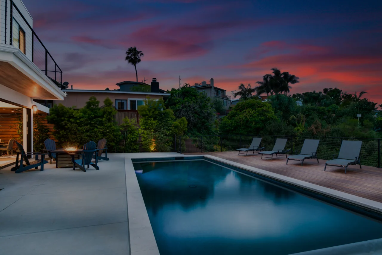Luxury San Diego property manager reviewing revenue metrics at a modern coastal home with illuminated pool and sunset patio