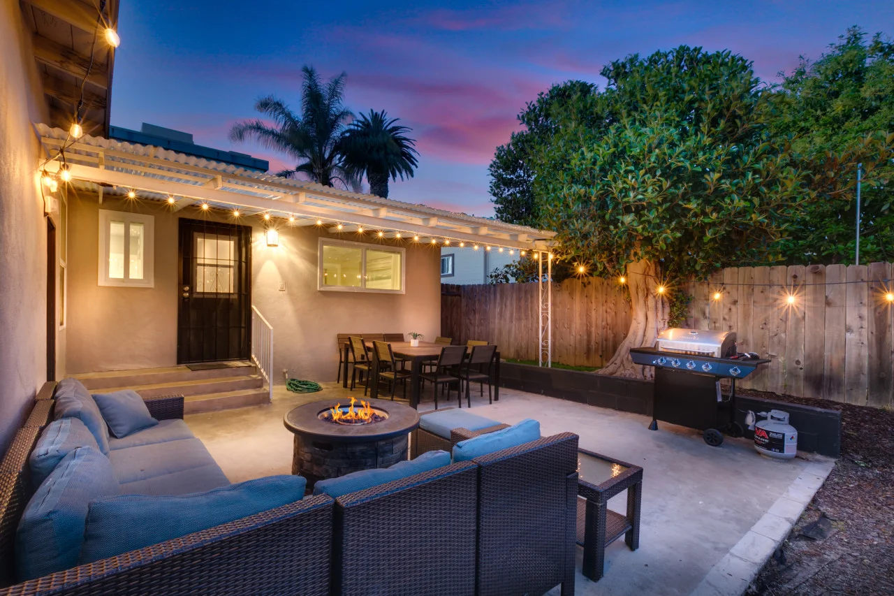 Backyard patio with fire pit, outdoor seating, and grill at twilight in San Diego