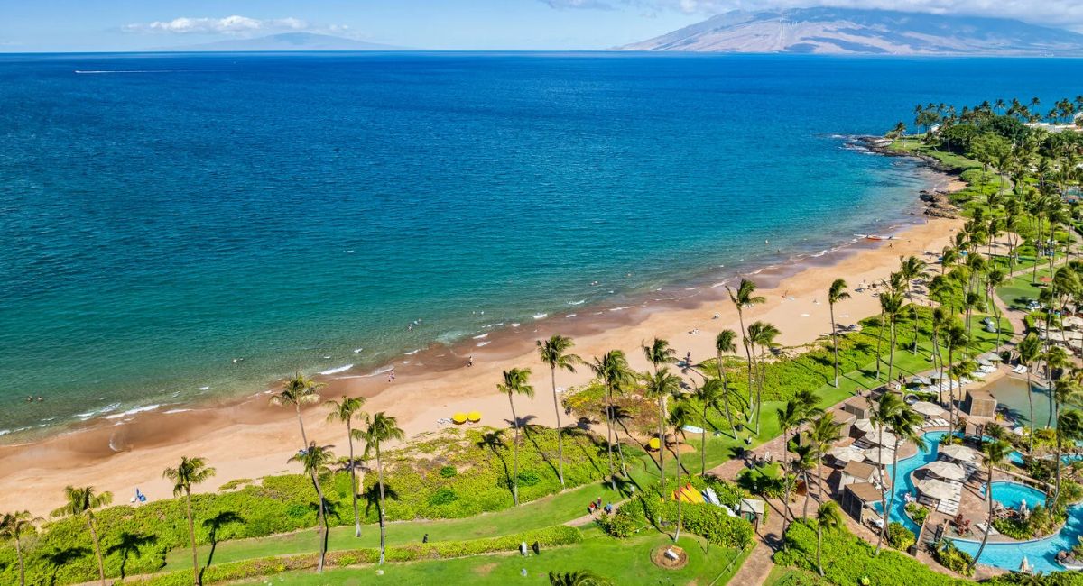 An aerial shot of Wailea beach, palm trees, blue water and the resorts in the area on a beautiful and sunny day