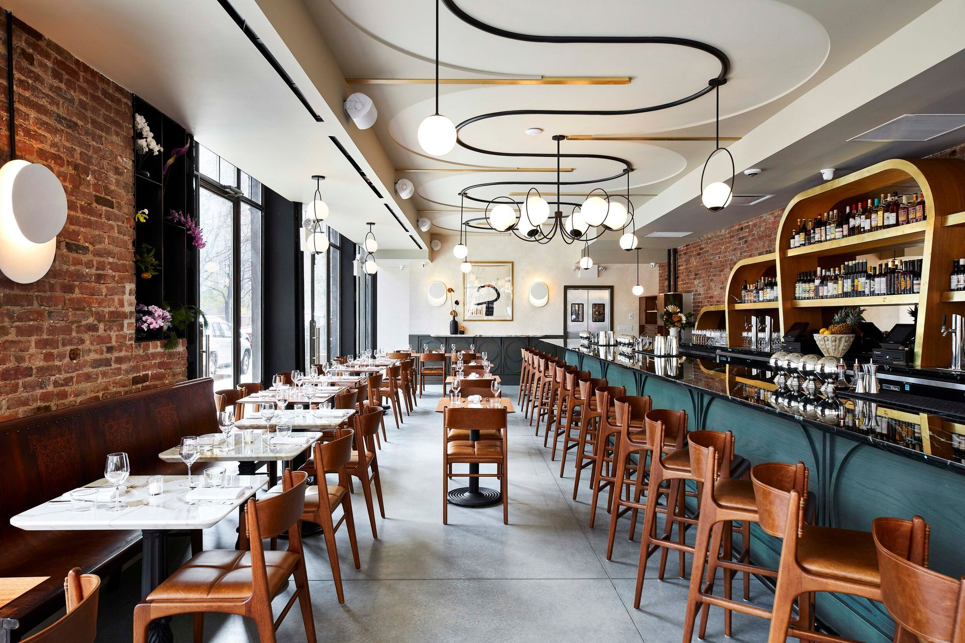 Restaurant interior with brick walls, tables, bar seating, and stylish lighting.