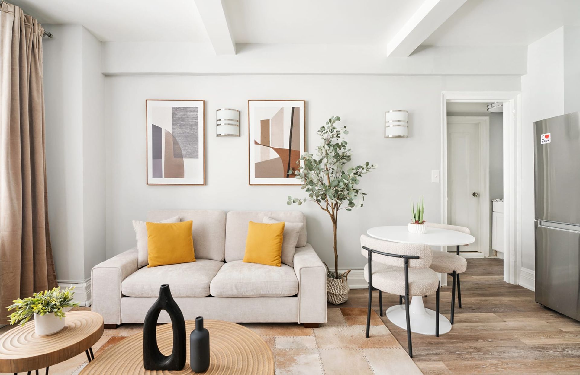 Cozy living room with a beige sofa, round table, framed art, and wooden floors.