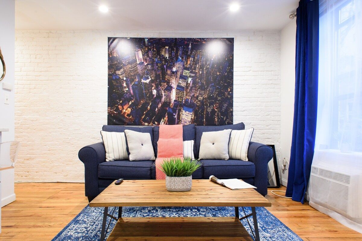 Living room with blue couch, large artwork, wooden coffee table, blue rug, and brick wall.