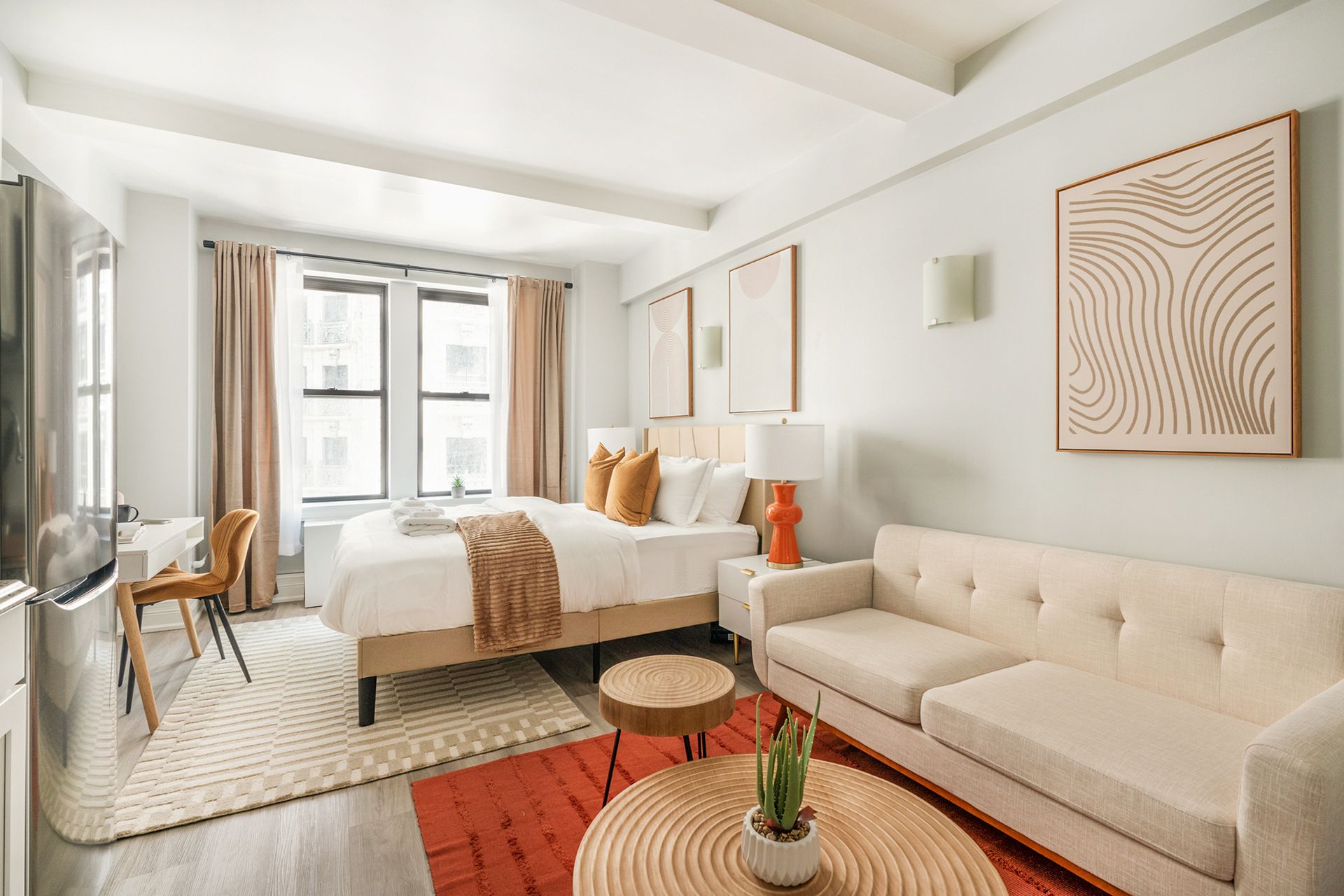 Bright, modern studio apartment with bed, sofa, small coffee table, and orange rug.