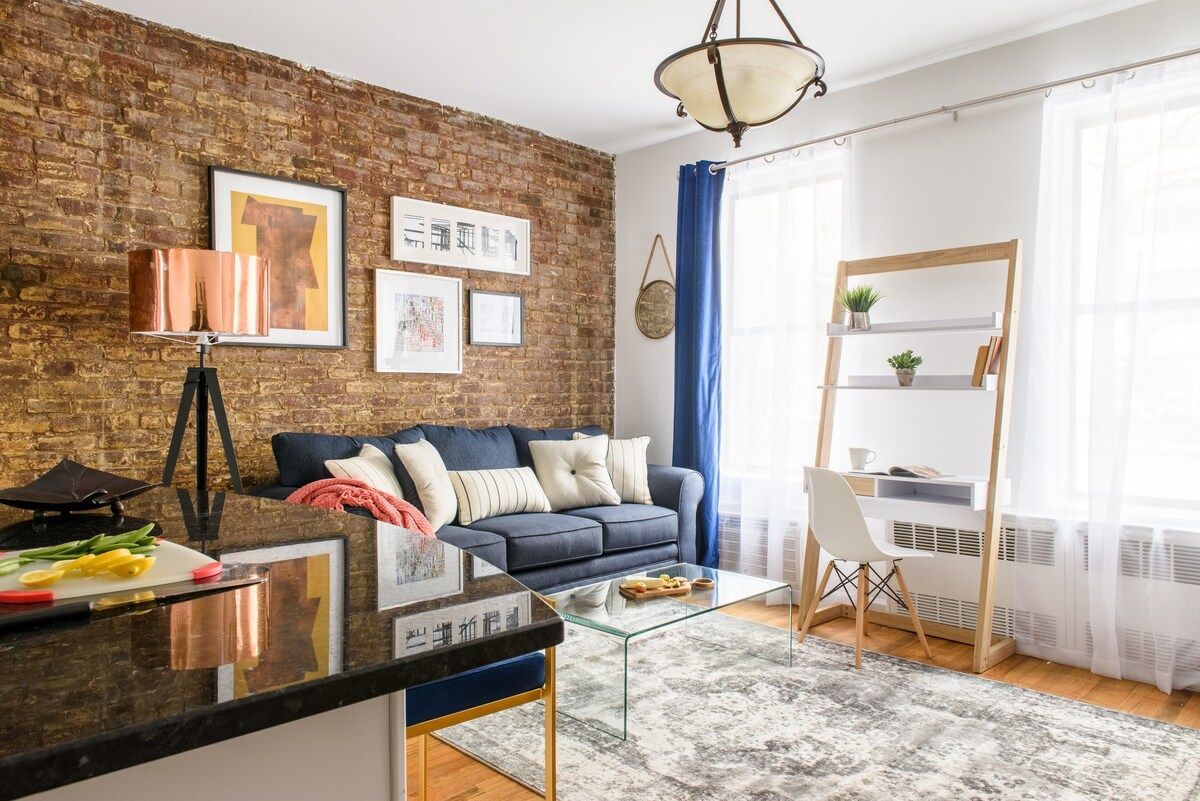 Cozy living room with brick wall, blue sofa, rug, and desk by window.