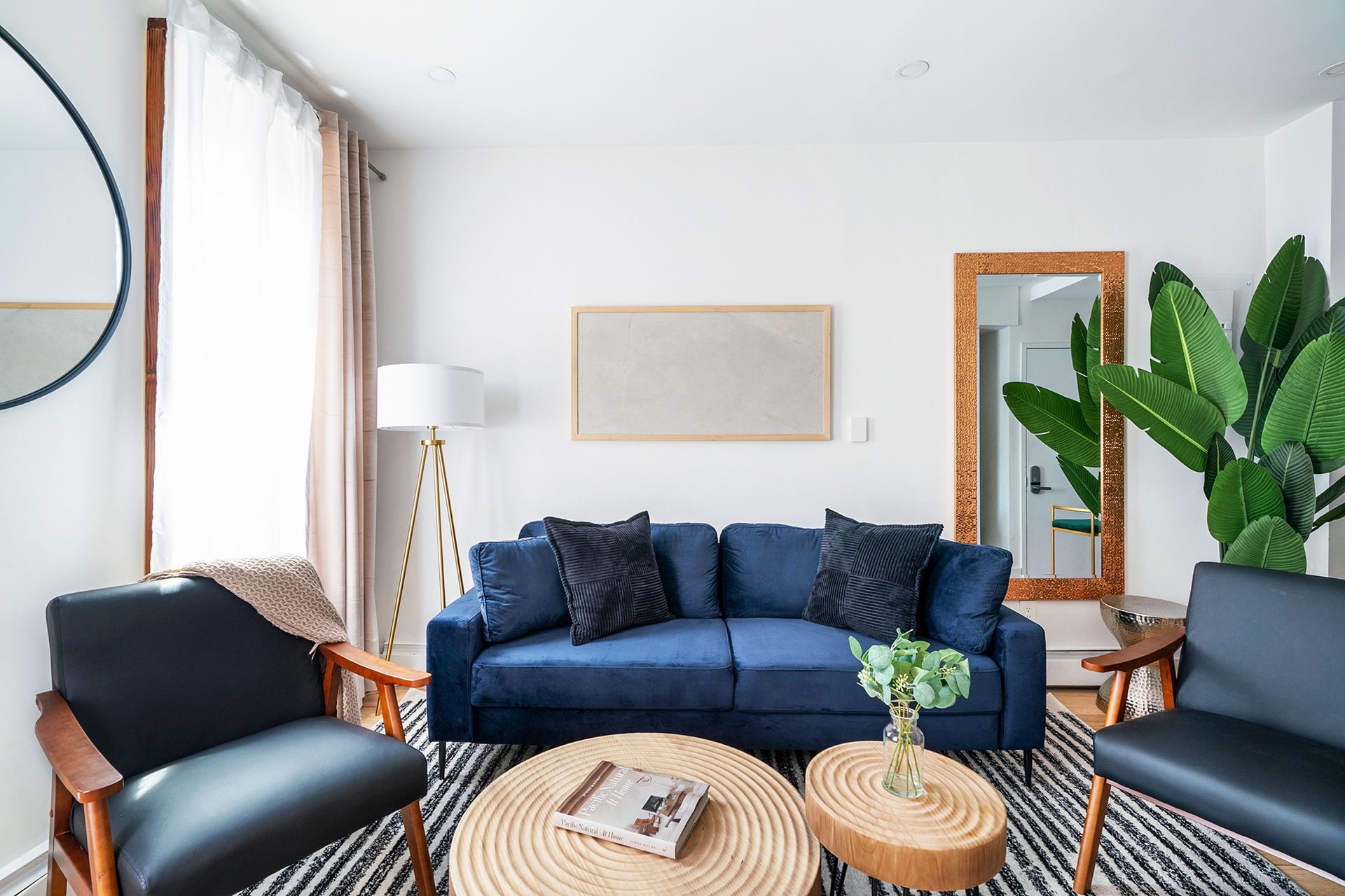 Living room with a blue couch, two black chairs, and two wooden coffee tables on a striped rug.