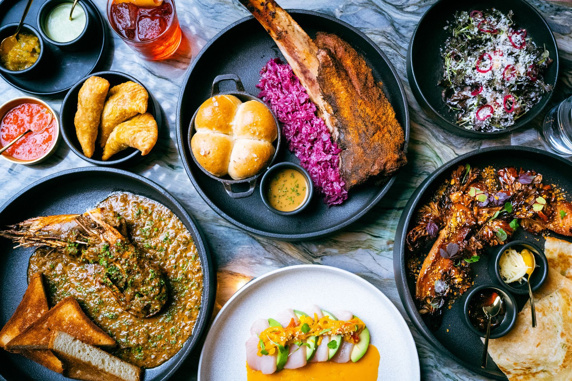 A table laden with diverse dishes, including meat, seafood, and sides, displayed on black plates.