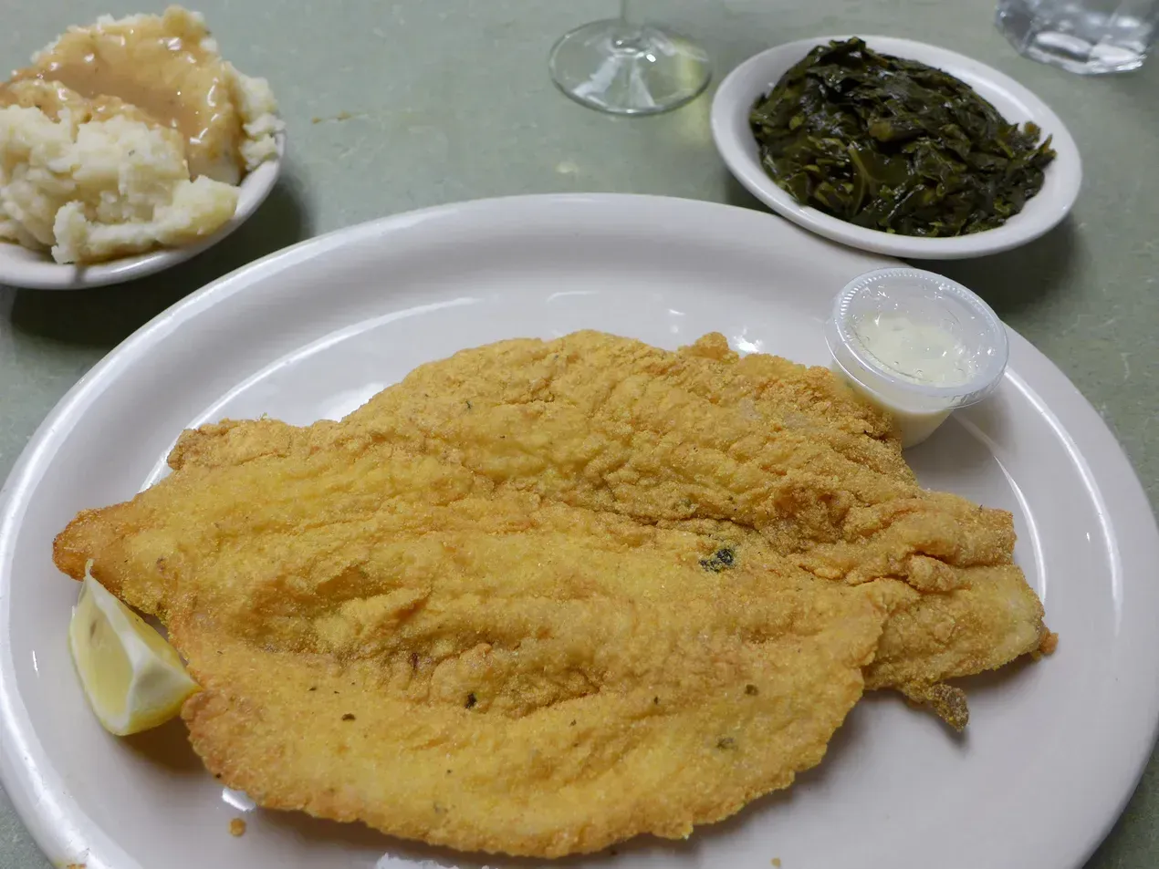 Fried fish with sides of mashed potatoes and collard greens.