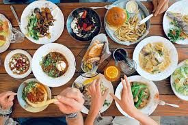 Overhead shot of a wooden table laden with various dishes, with hands reaching in, suggesting a shared meal.