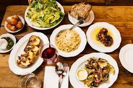 Table set with various dishes including pasta, salad, and bread, served on white plates.