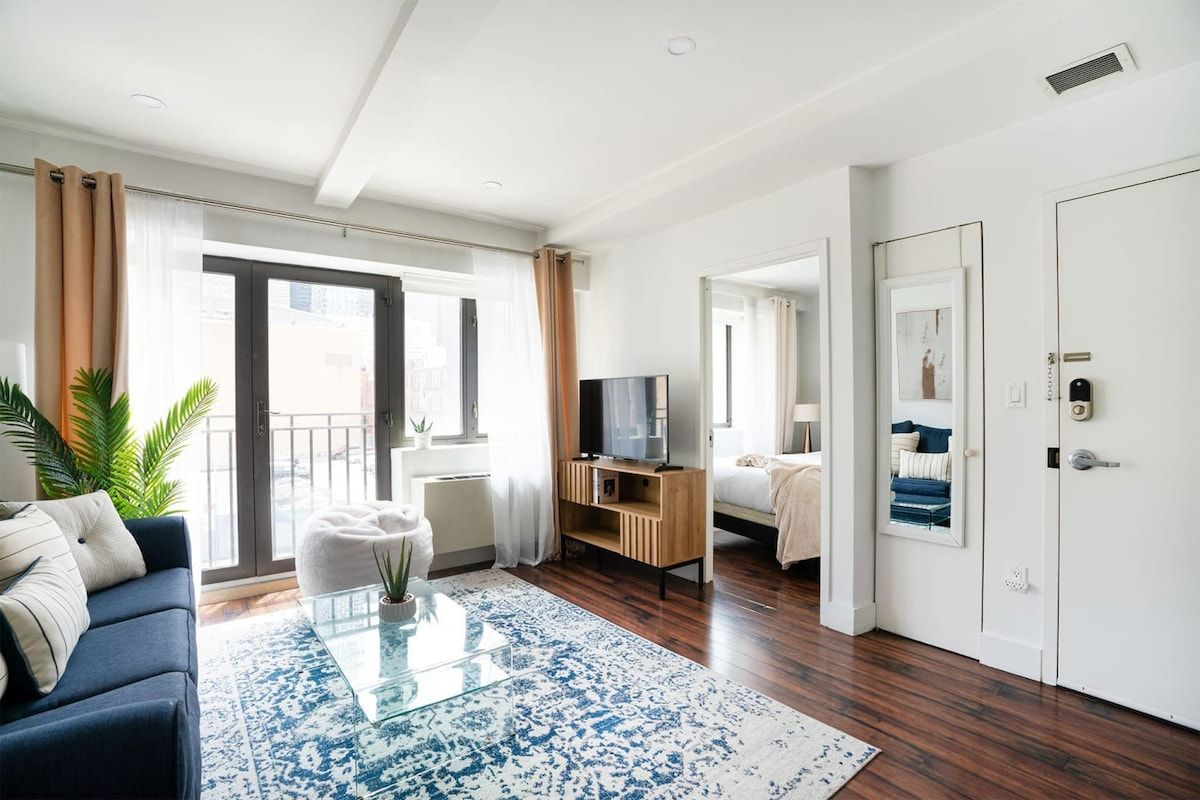 Living room with blue sofa, TV, rug, and view to the bedroom, bright and airy.