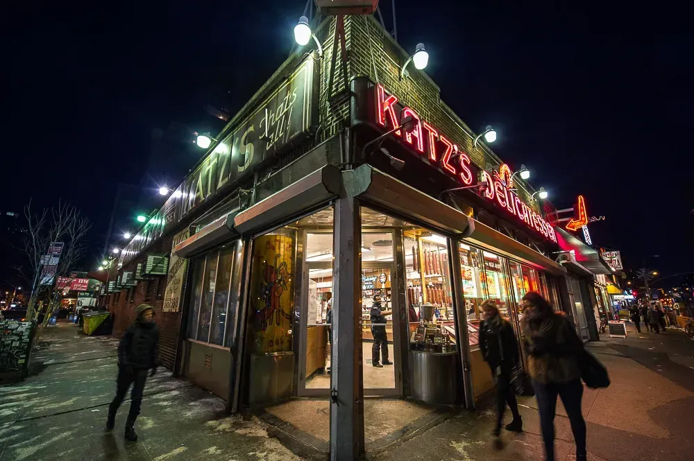 Katz's Delicatessen at night, with neon sign and people on sidewalk.