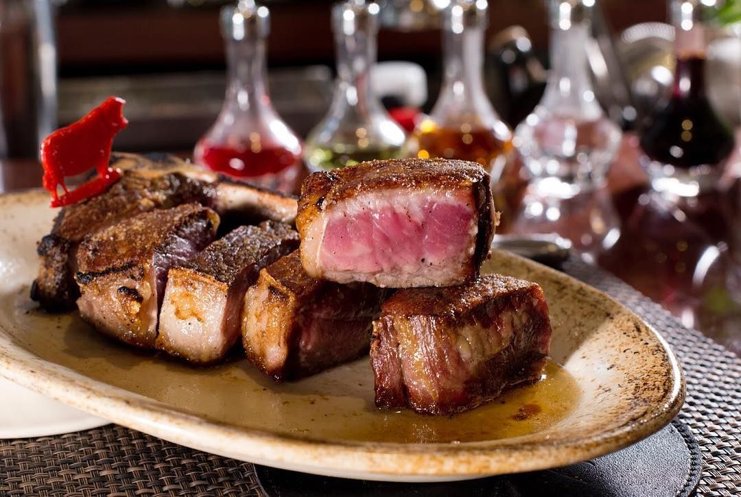 Grilled steak cubes on a plate, medium-rare cut visible. Several sauces in glass bottles are in the background.